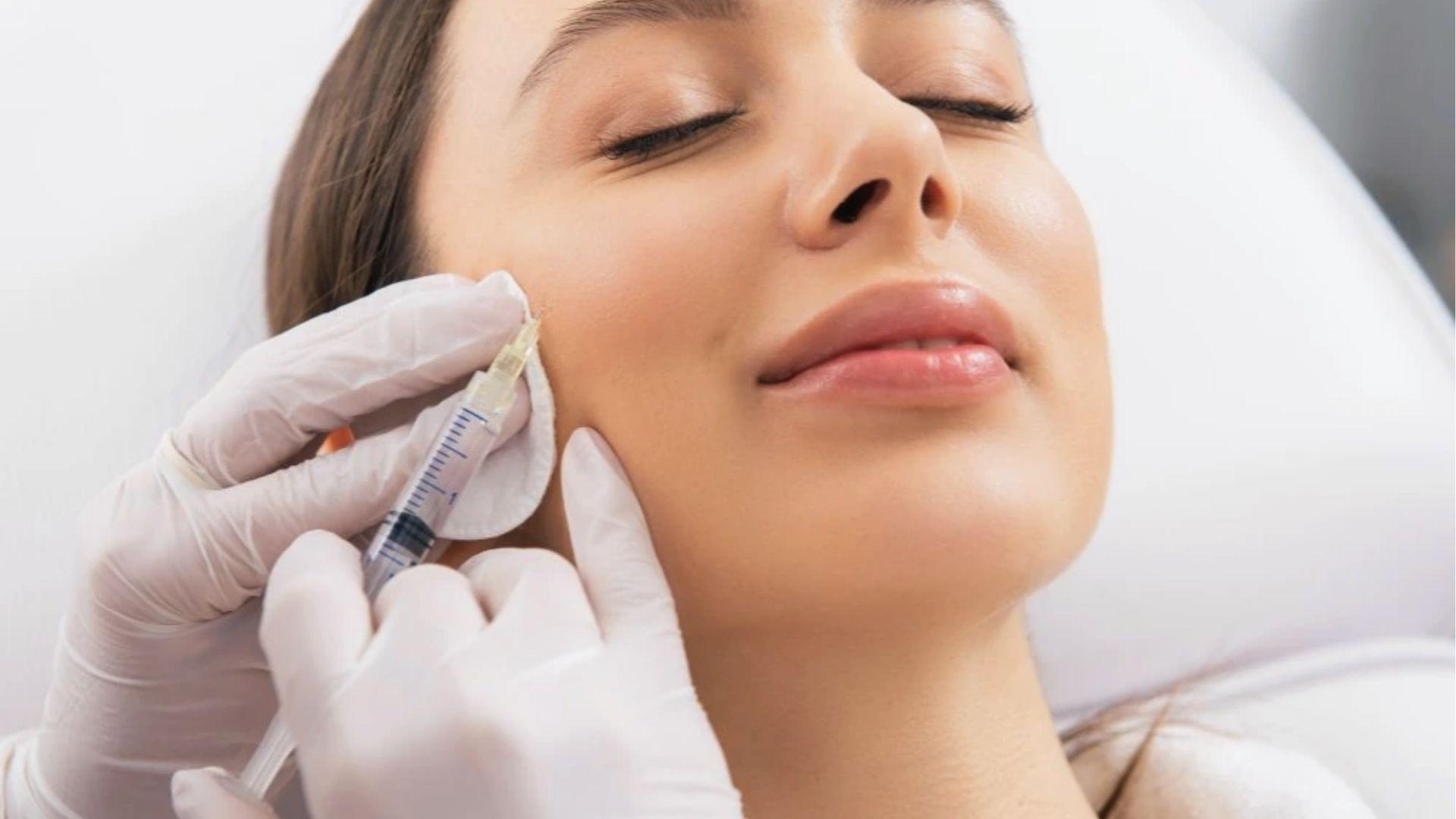 Patient with eyes closed getting dermal filler injected into cheek by doctor wearing white gloves