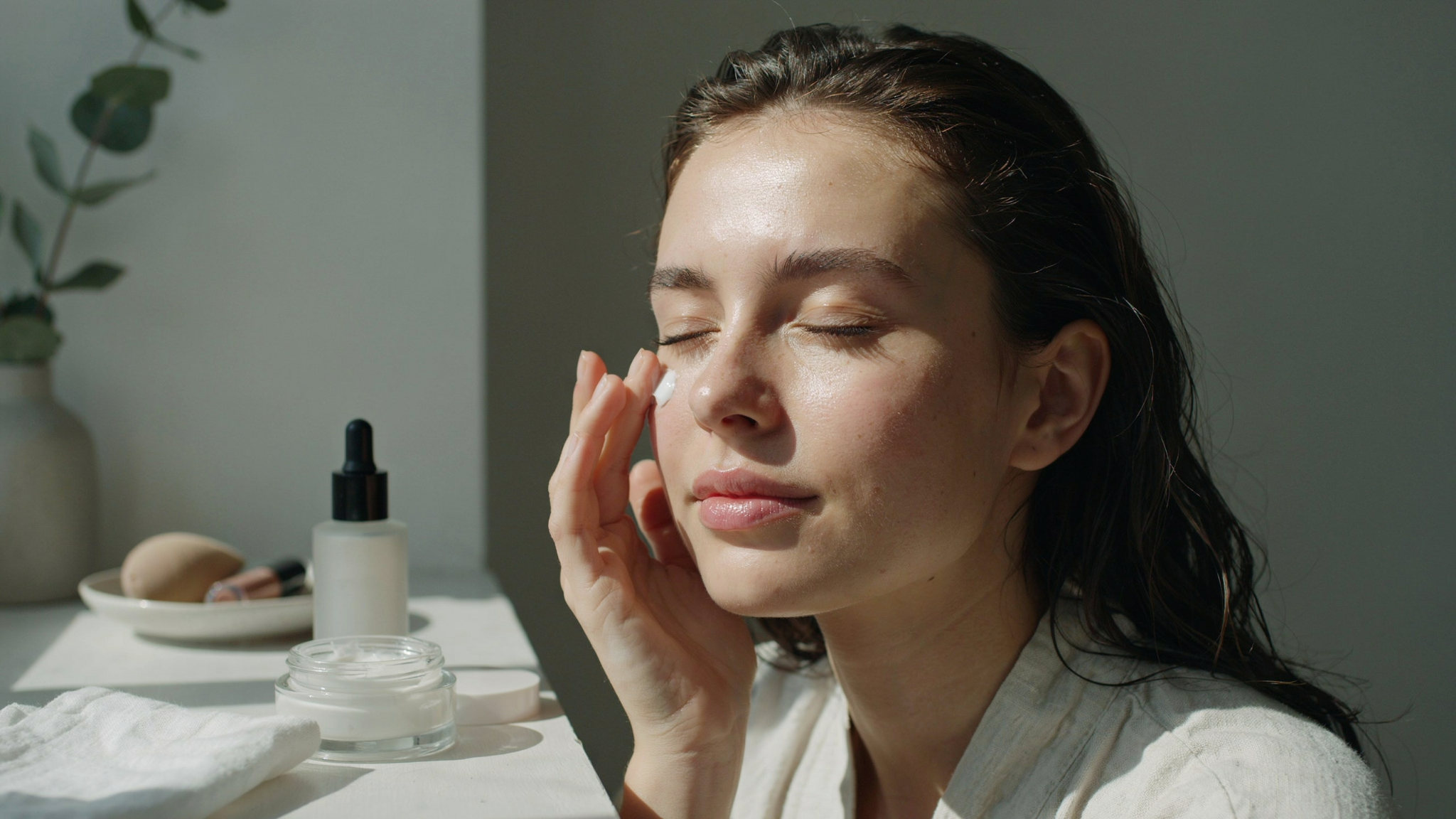 Woman applying moisturizer to clean skin before concealer application.