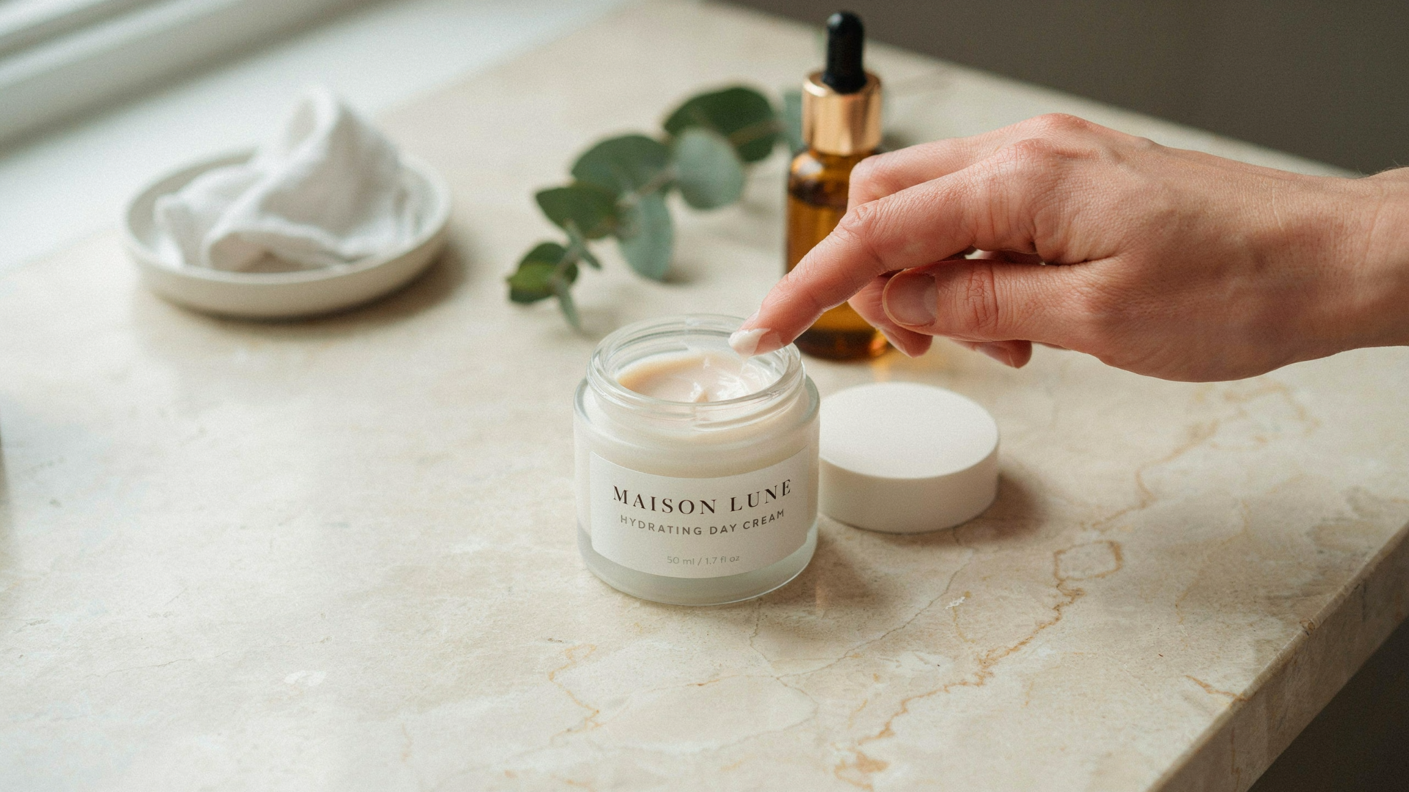 Natural face moisturizer cream being applied from jar with simple clean skincare setup on minimal bathroom counter.