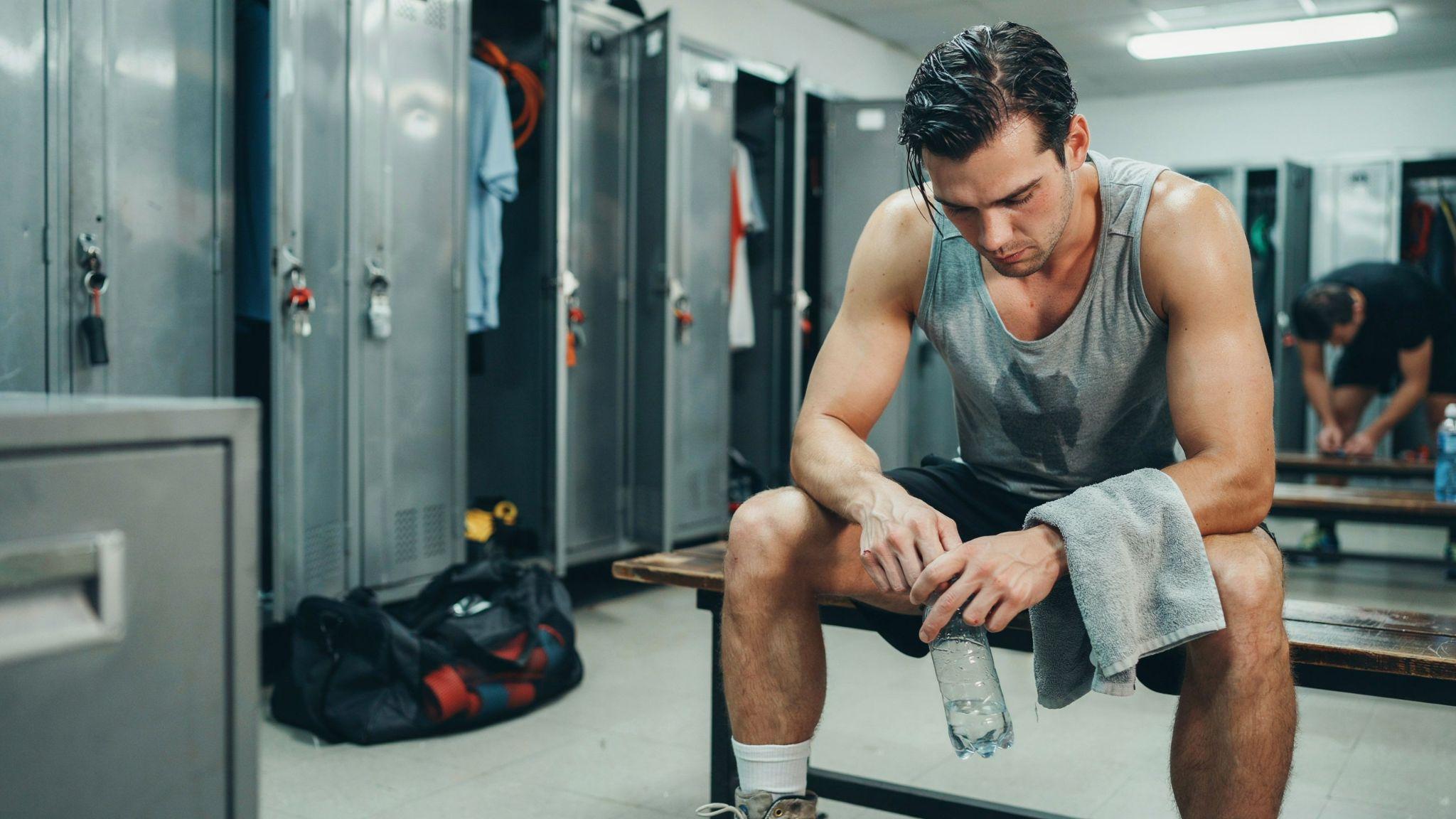 "Tired gym-goer sitting in locker room reflecting after intense workout in realistic lighting"