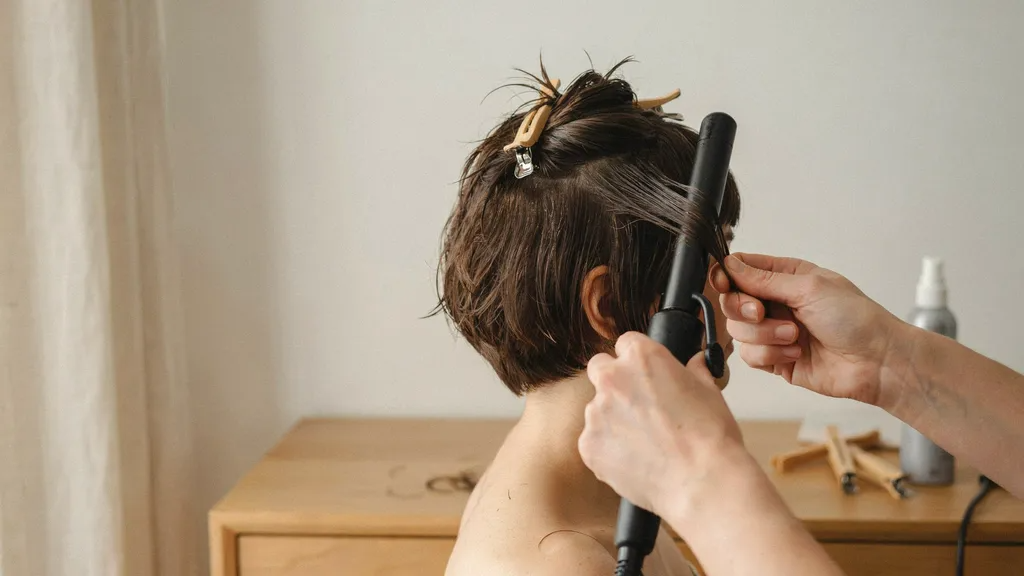 Person wrapping short hair around curling iron barrel to create defined curls.
