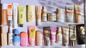 Flat lay of 20 clean beauty tinted moisturizers with SPF from brands like COOLA, Kosas, ILIA, Saie, and Tower 28.