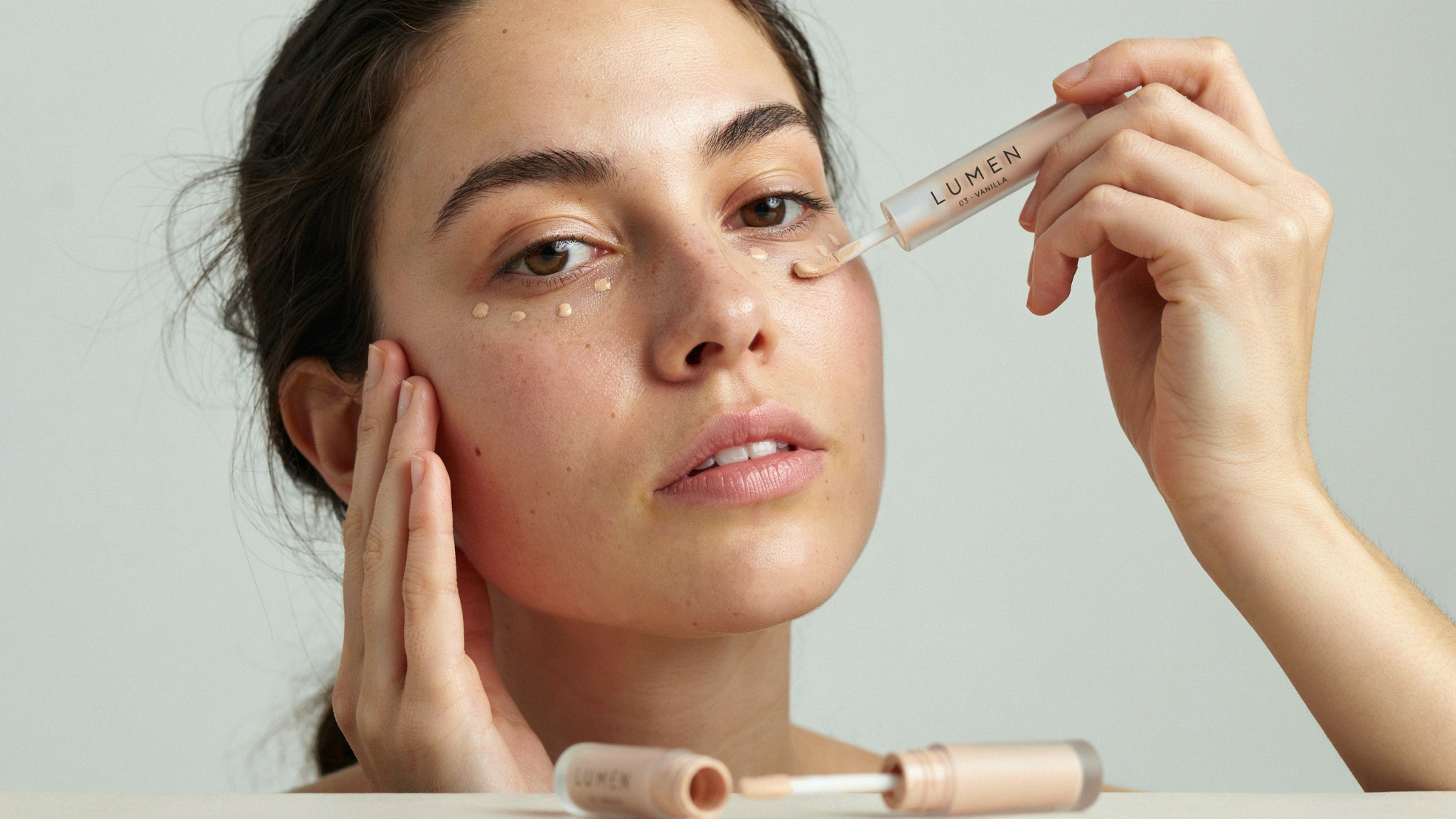 Woman applying small dots of concealer under her eyes to cover dark circles.