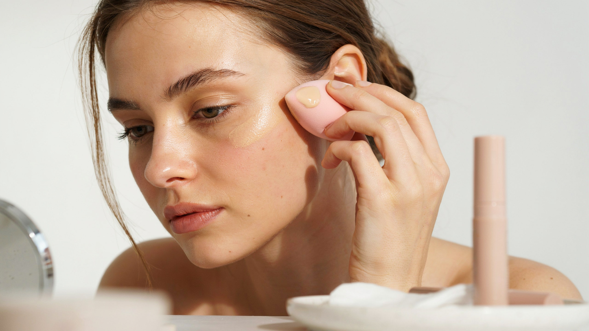 Woman blending concealer into the skin with a makeup sponge using gentle tapping motions.
