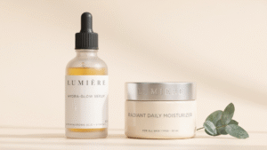 Lumière Hydra-Glow Serum dropper bottle and Radiant Daily Moisturizer jar displayed on a beige surface with eucalyptus.