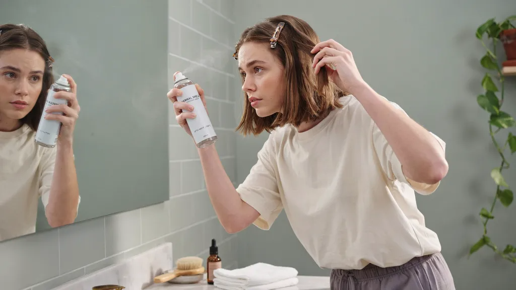 Woman with short brown bob applying heat protectant and sectioning hair before styling.