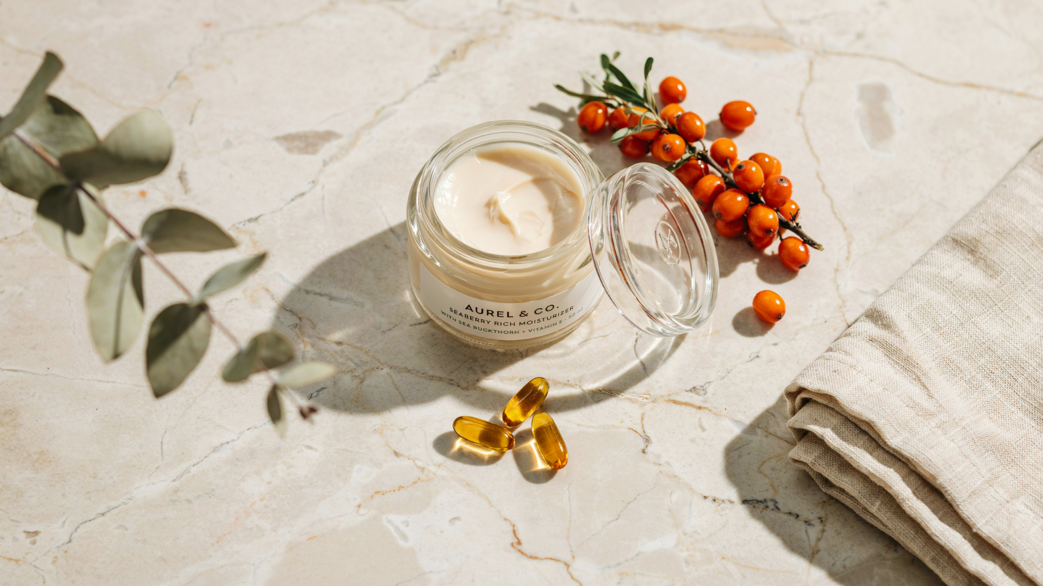 Seaberry face moisturizer with sea buckthorn berries and vitamin E capsules arranged on a clean warm toned background.