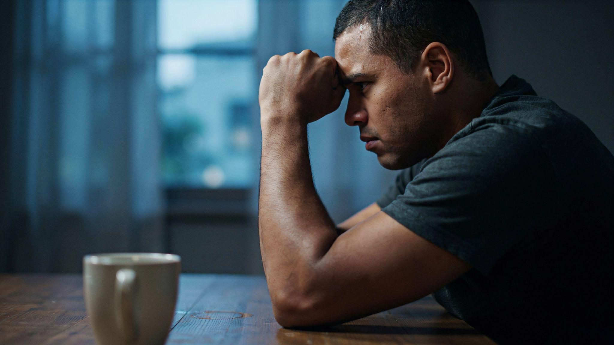 Stressed man leaning on dark elbow at table, showing skin discoloration concern