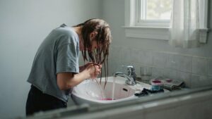 Person rinsing faded semi-permanent hair dye from hair in a realistic home bathroom setting.