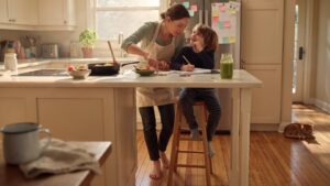 A woman and a child stand together at a kitchen counter, engaged in a cooking activity.