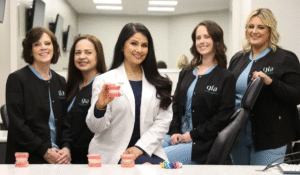 A group of women in scrubs smiles while holding cups filled with pink toothpaste, showcasing a dental health initiative.