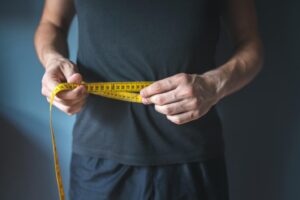 A man measuring his waist with a tape measure, focusing on his midsection for accurate sizing.
