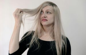 A woman with long hair is gently combing her hair, focusing on smoothing out tangles.