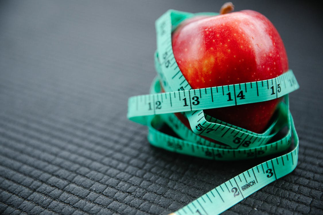 A red apple wrapped in a measuring tape, symbolizing health and nutrition measurement.
