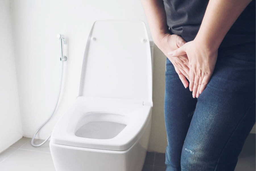 A woman is resting her hands on the toilet, appearing contemplative in a bathroom setting.