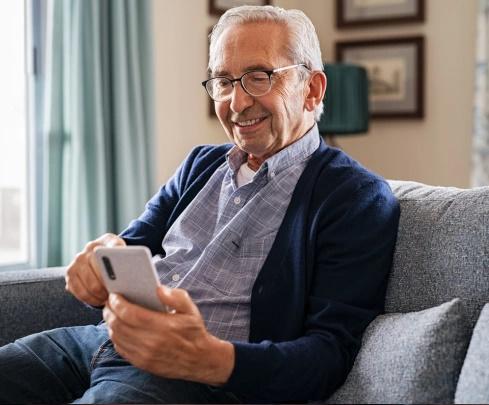 An older man sitting on a couch, focused on using his smartphone.