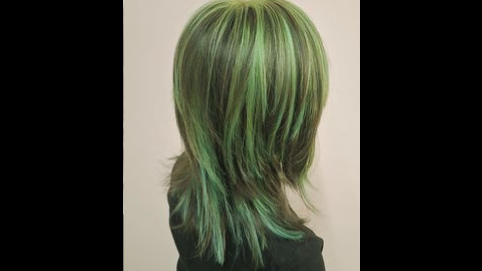 Rear view of a person with bobbed hair showing bright green highlights over a dark base color.