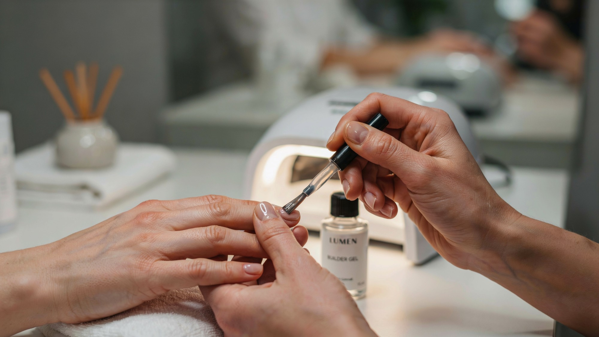 Thick builder gel being applied to natural nails in a salon.