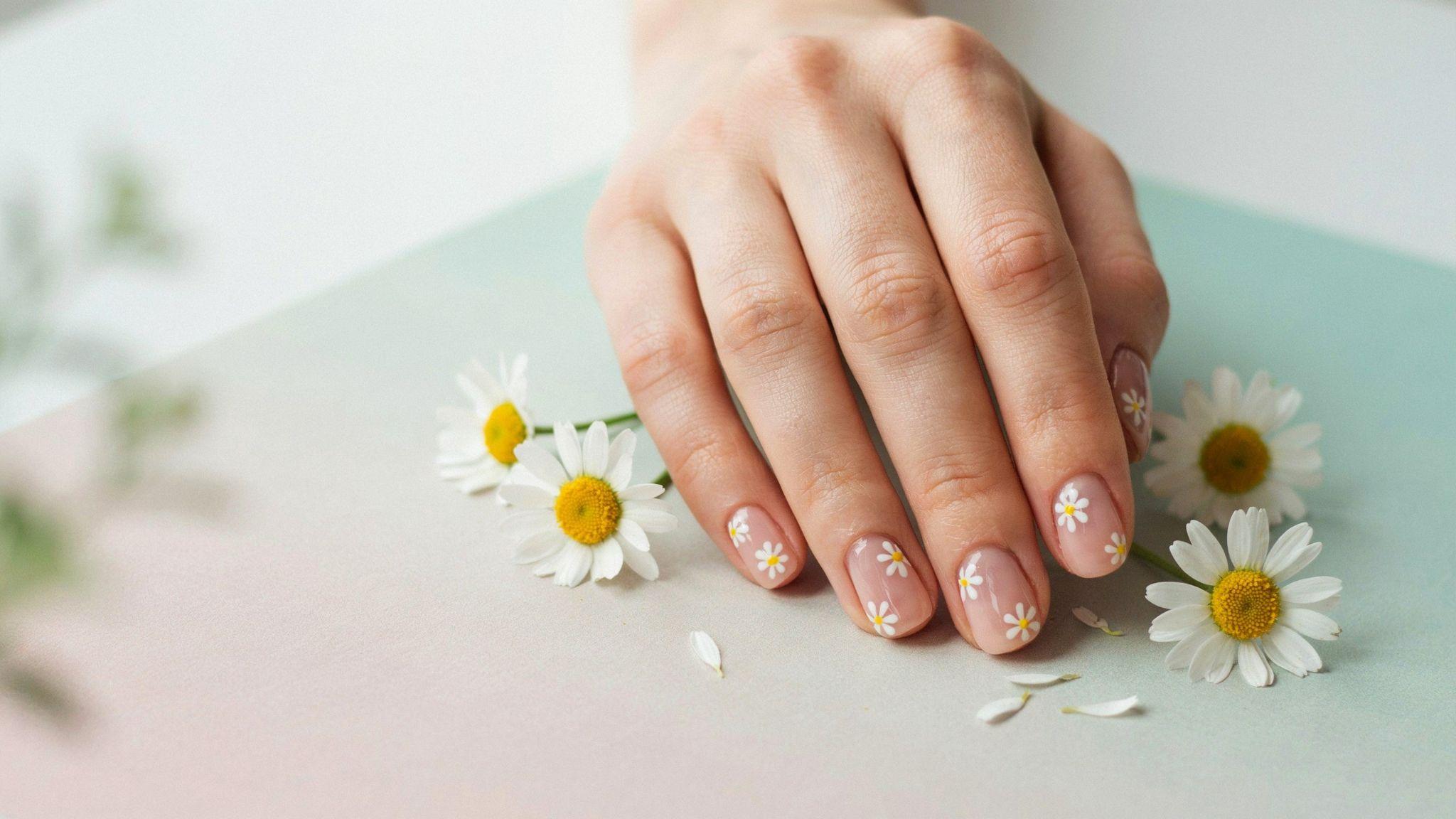 Nude short square nails decorated with tiny white daisies creating a fresh feminine floral manicure design.