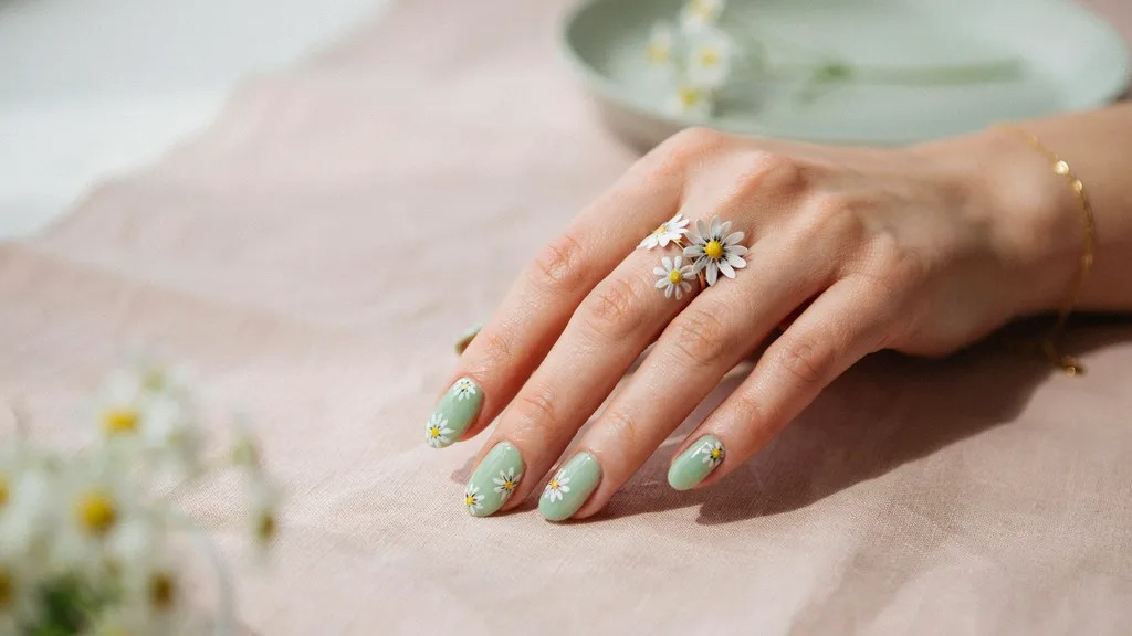 Light green nails decorated with white floral nail art.