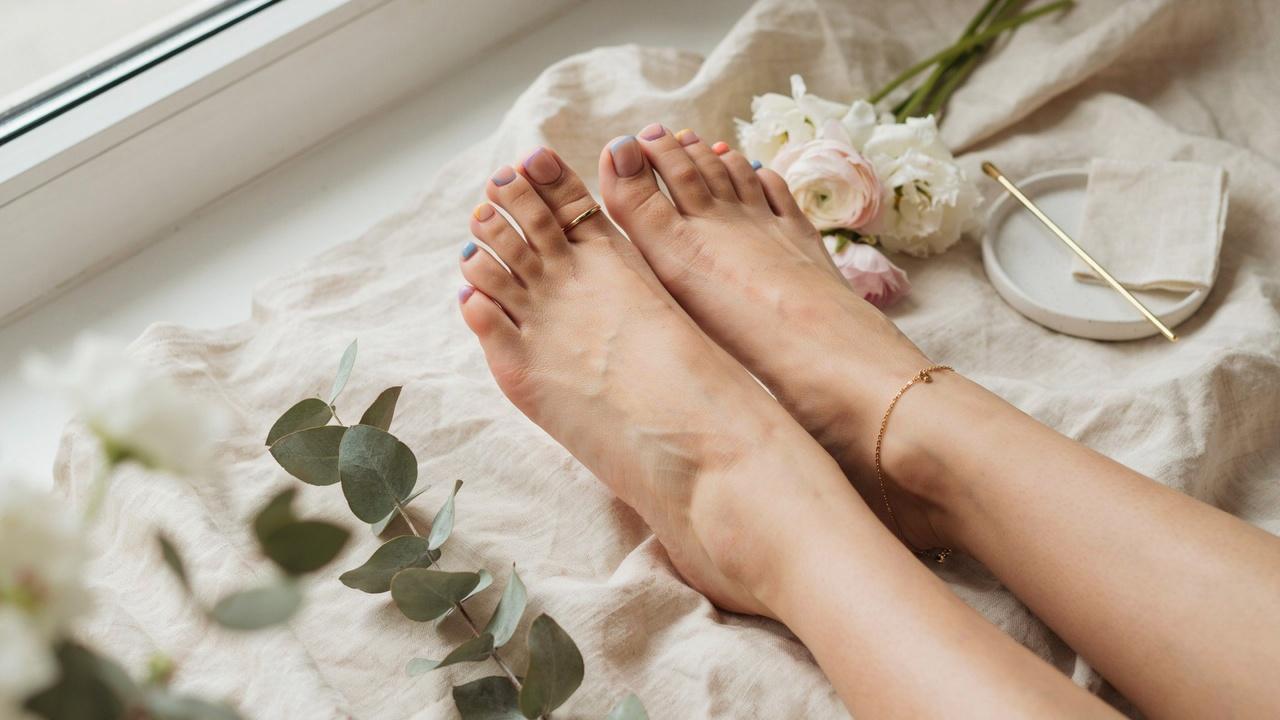 Beautifully groomed feet showcasing a colorful French tip pedicure with pastel accents in an elegant spa-inspired setting.