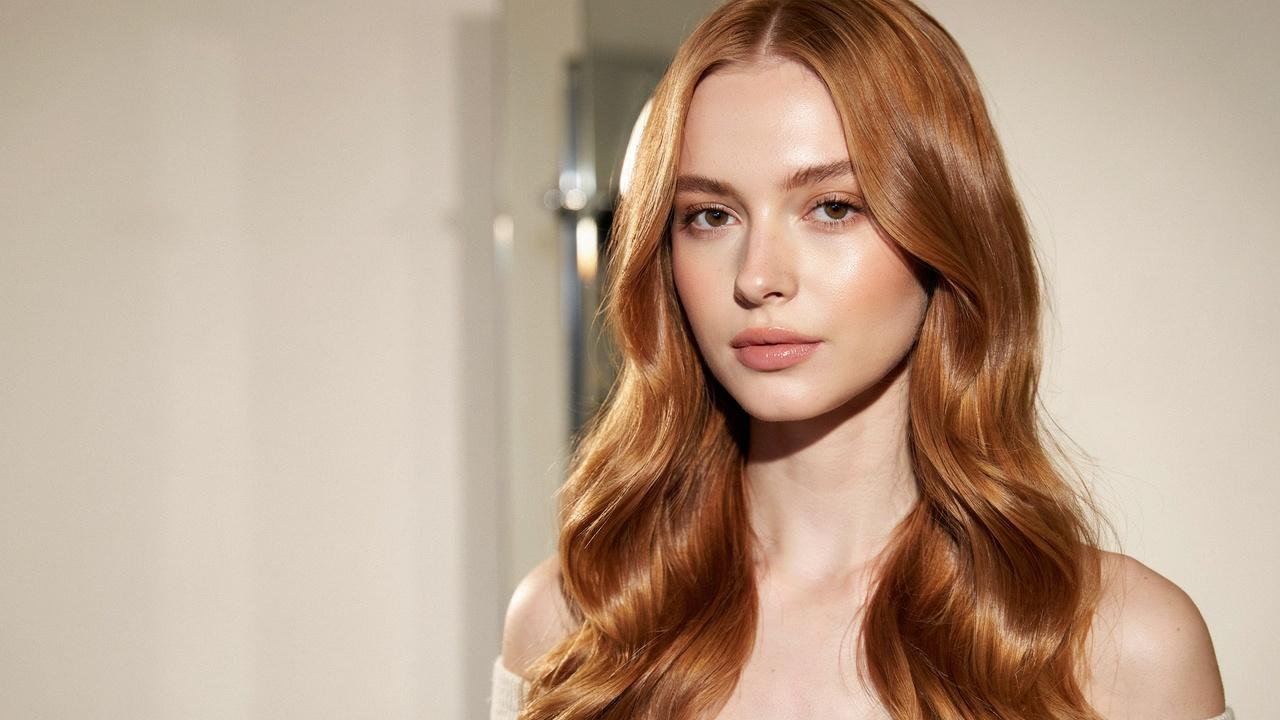 A woman with shiny, vibrant copper-colored wavy hair showcasing the warm orange-red tones of copper hair color.