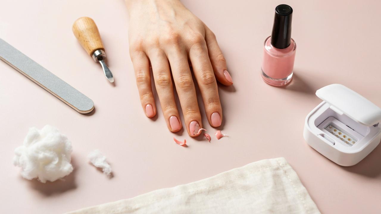 Close-up of a hand with peeling gel nail polish surrounded by manicure tools and gel nail products.