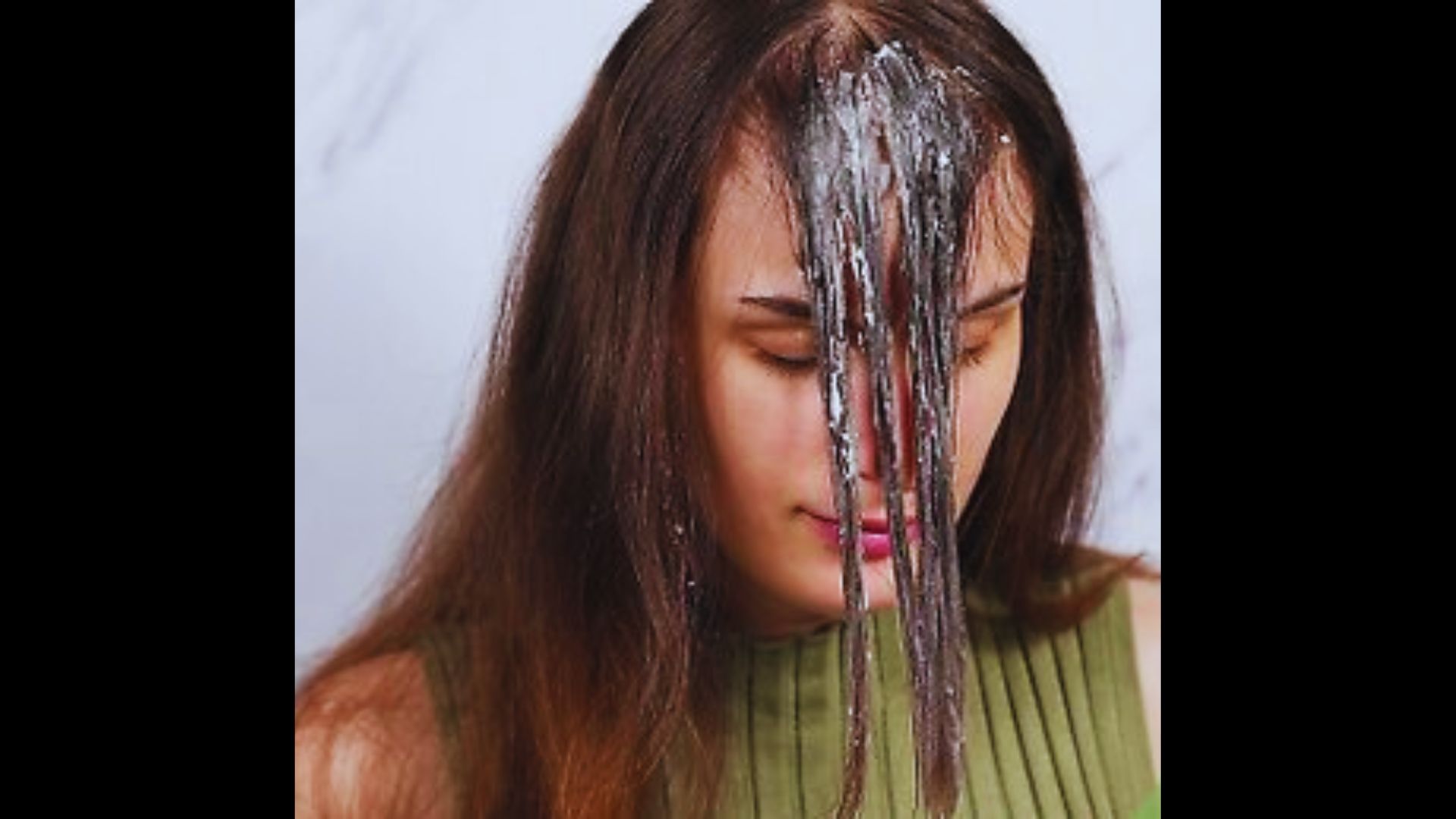 A close-up of a woman with dark hair getting water or a clear paste poured over her head.