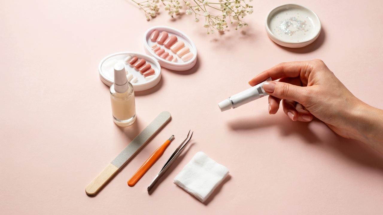 A tube of super glue and a bottle of nail glue displayed beside press-on nails and manicure tools for comparison.