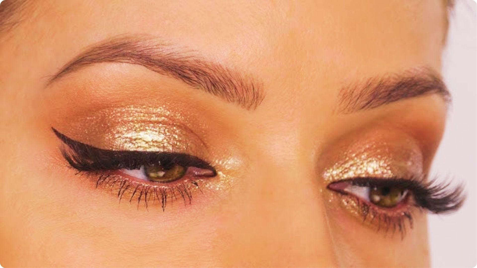 Close-up of hazel eyes with glittery gold eyeshadow, bold winged liner, and full lashes for a soft glam bridal eye look.