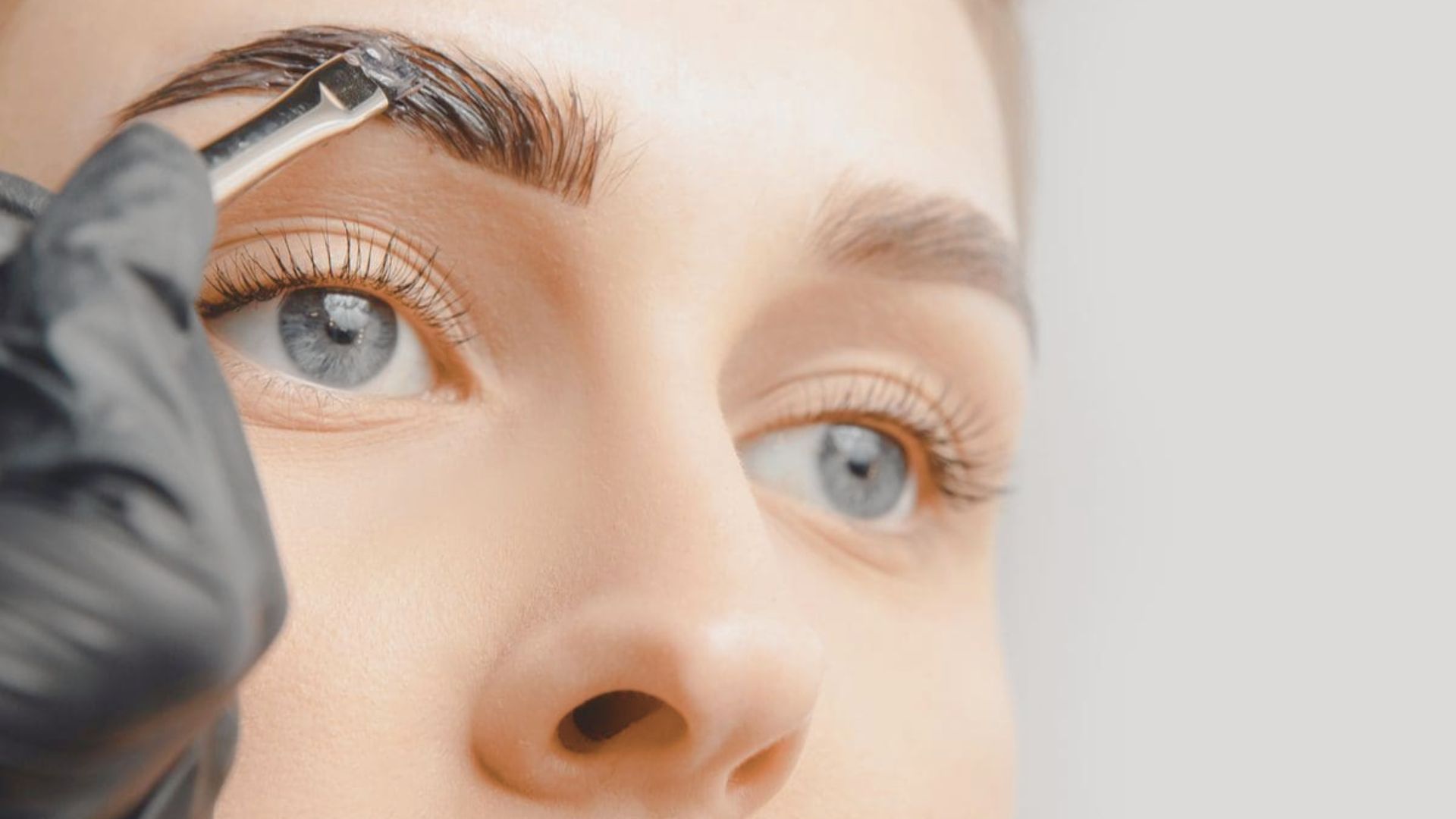 A beautician carefully styles a woman's eyebrows in a well-lit salon, showcasing beauty tools and products.