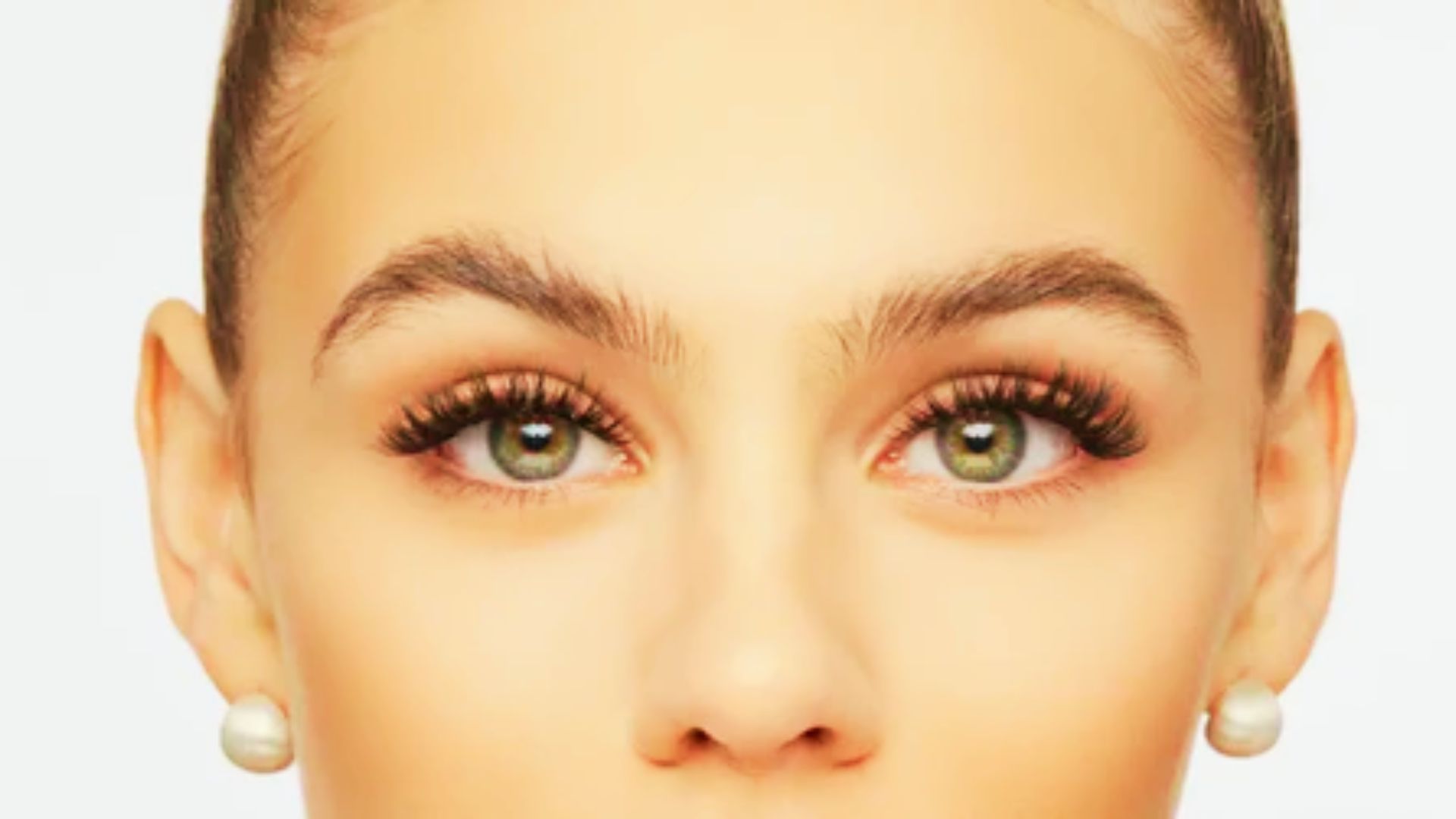 Close-up of a bride with wispy eyelashes, slicked hair, and pearl stud earrings.