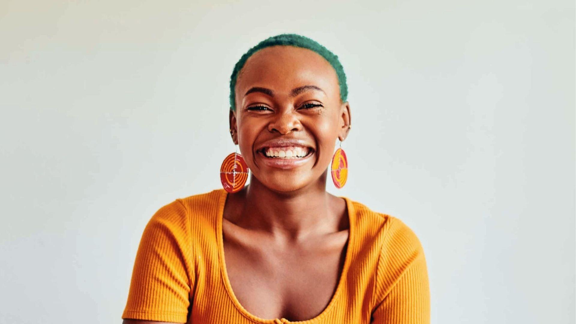 Smiling woman in yellow top, short teal cut with shaved sides, bold round earrings