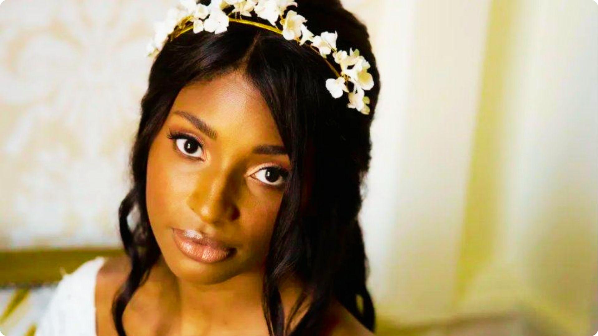 Bride wearing a white floral headband with loose curls, showcasing soft natural wedding makeup with neutral eyeshadow, defined lashes, and glossy nude lips.