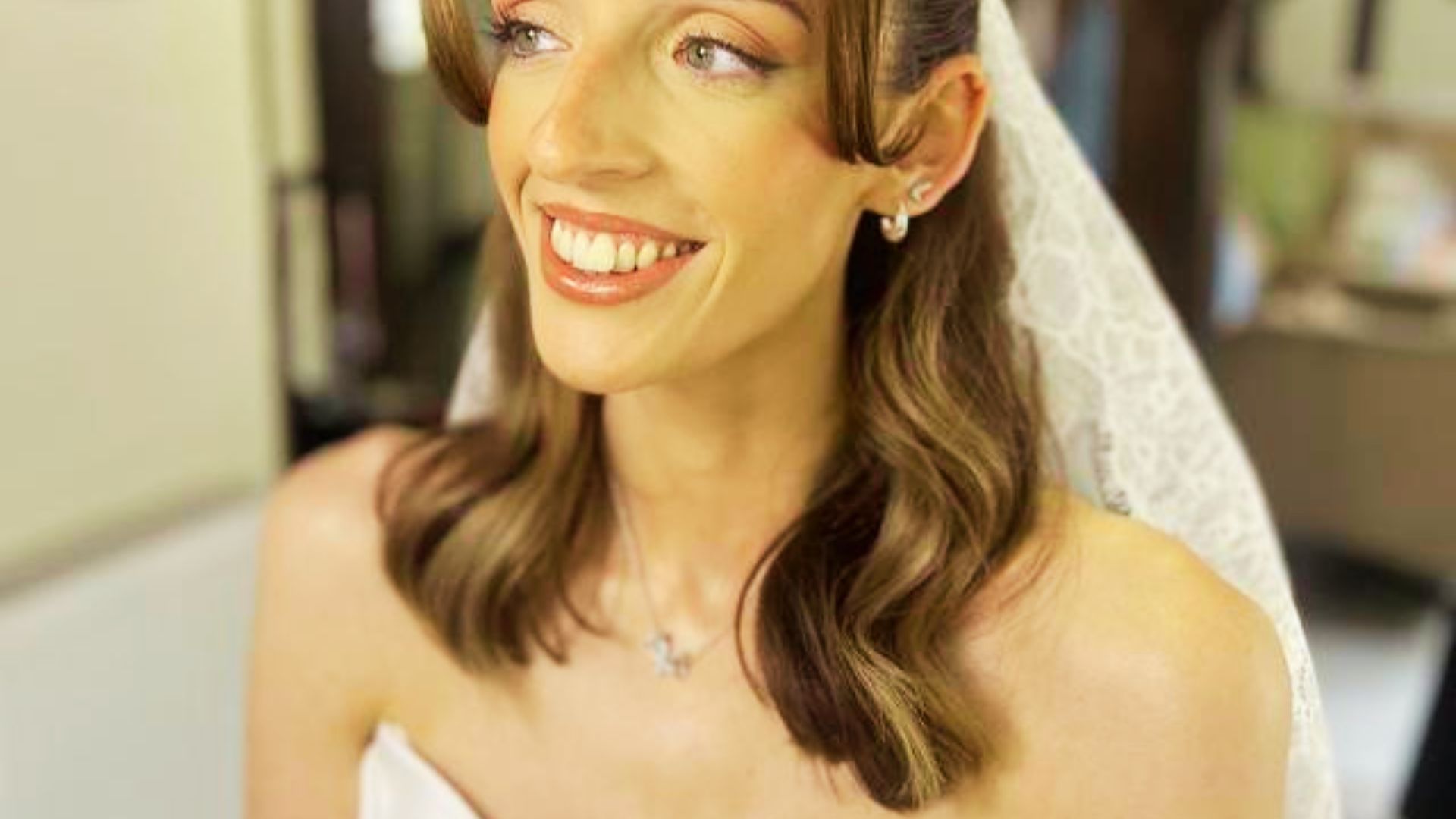 Brunette bride in a lace veil with side-swept waves and delicate jewelry.