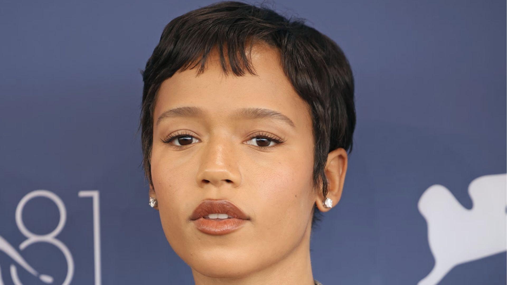 Headshot of woman with sleek pixie cut, wispy bangs, studs, blue event backdrop