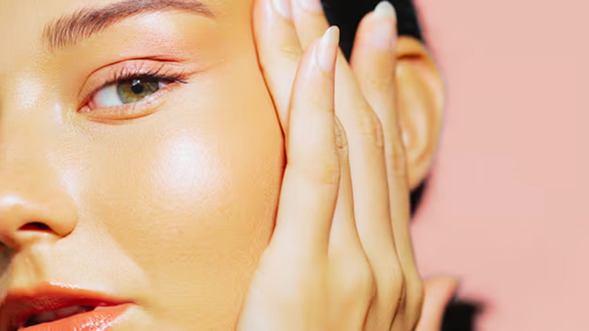 Cropped shot of a model’s face with hands framing her glowing cheek.