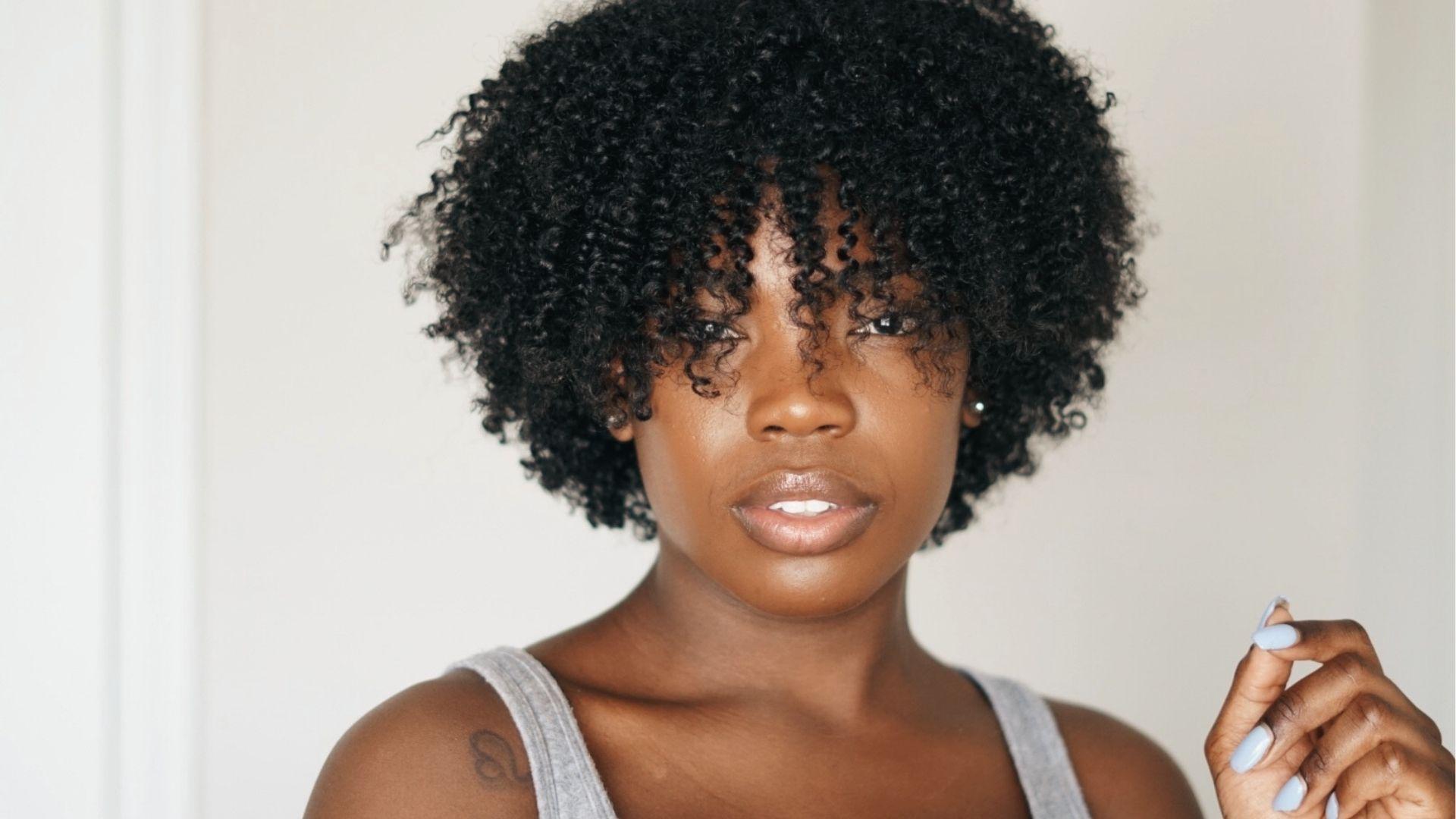 Woman with short twist style, soft bangs, gray tank top, blue nails, tattoo