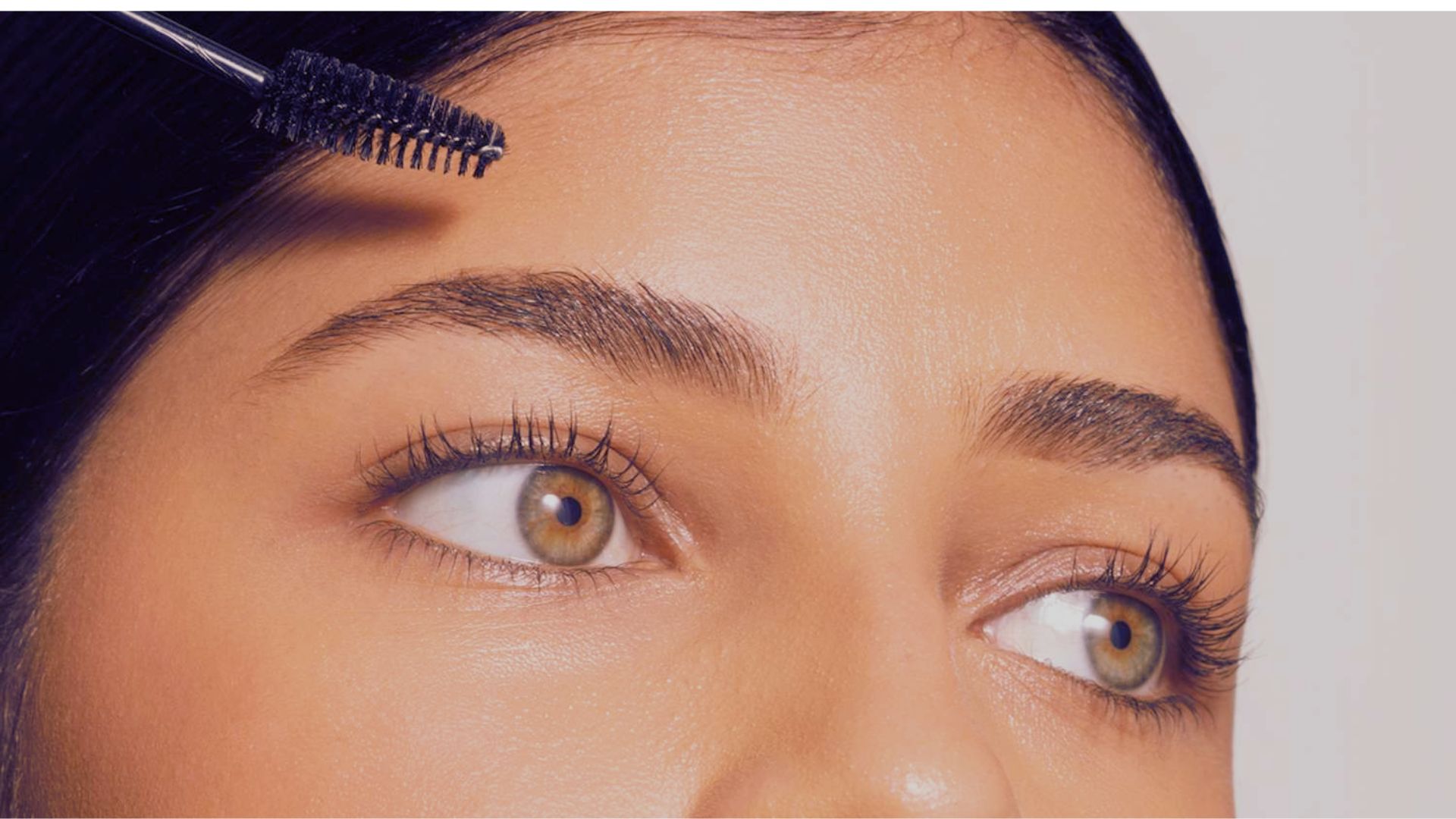 A woman carefully brushes her eyebrows with a makeup brush, focusing on enhancing their shape and definition.