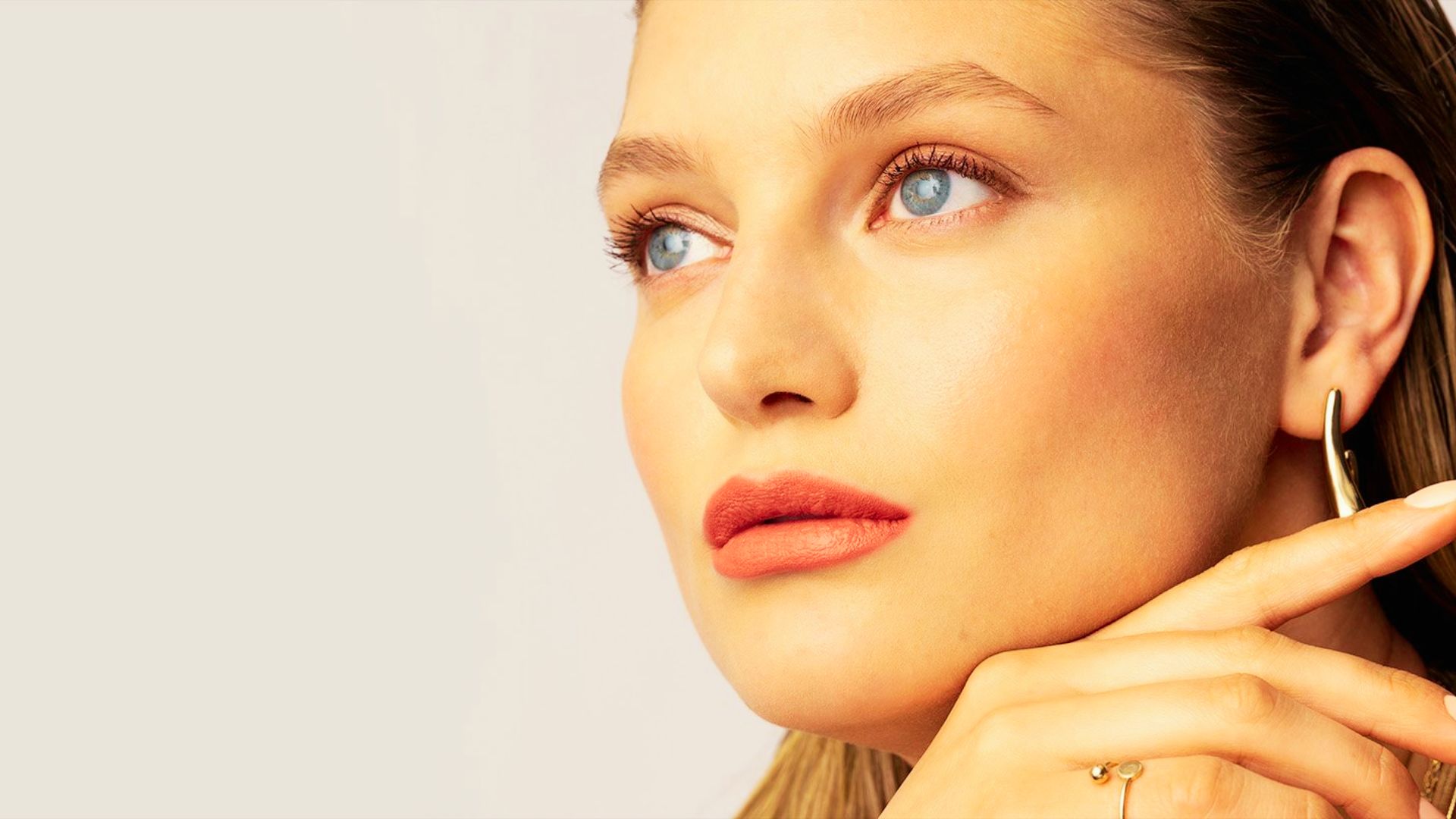 Woman with soft natural makeup featuring peach-toned lips, defined brows, and light mascara for a fresh-faced glow.